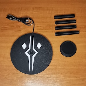 May include: A black circular charging pad with a white geometric design and a black USB cable. Four black metal legs are included.