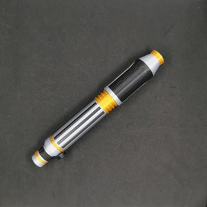 May include: A silver and black lightsaber toy with gold accents. The lightsaber is made of plastic and has a textured surface.