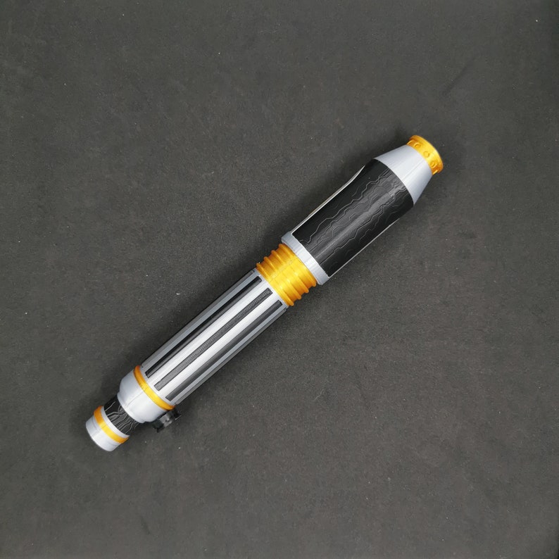 May include: A silver and black lightsaber toy with gold accents. The lightsaber is made of plastic and has a textured surface.