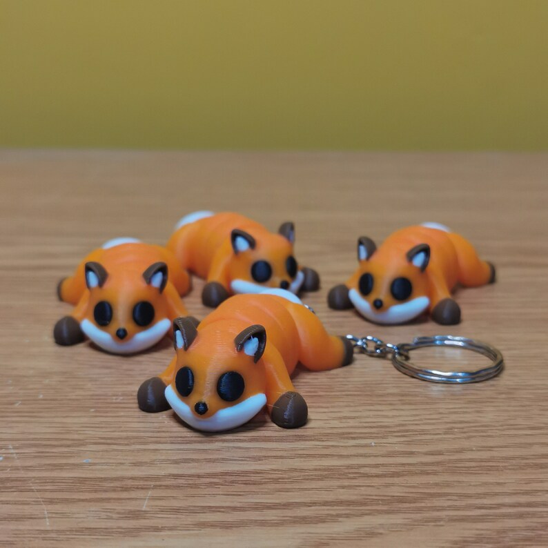 May include: Four orange and brown fox-shaped keychains with black eyes. One keychain is attached to a silver key ring.
