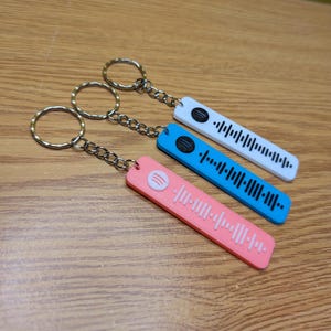 May include: Three keychains with different colored rectangular tags. Each tag has a Spotify logo and a black and white barcode. The keychains are attached to silver key rings.
