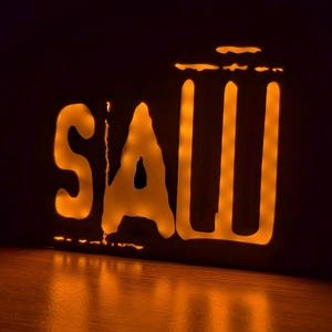 May include: A neon sign with the word "SAW" in white letters with a yellow glow. The sign is on a dark background.