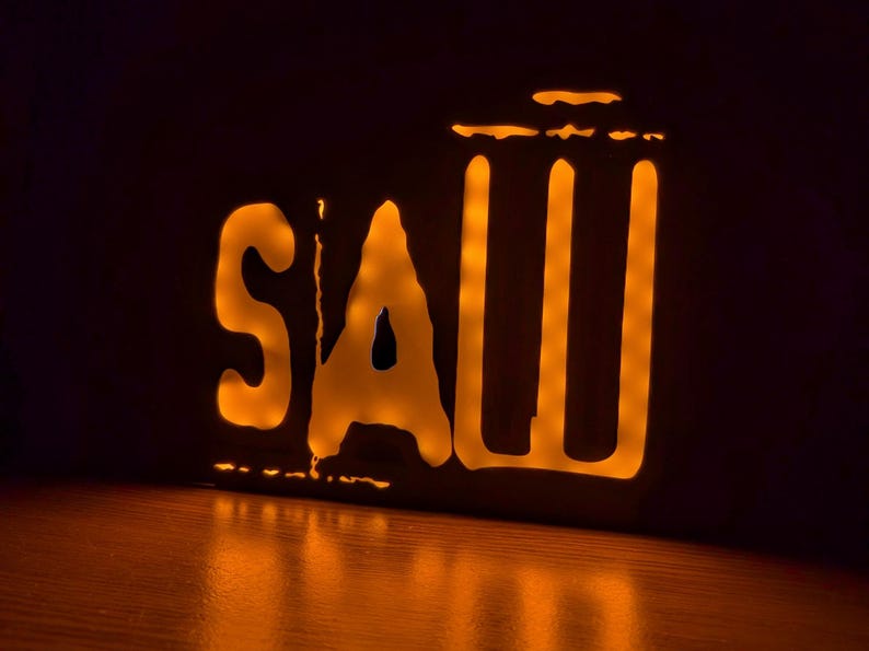 May include: A neon sign with the word "SAW" in white letters with a yellow glow. The sign is on a dark background.