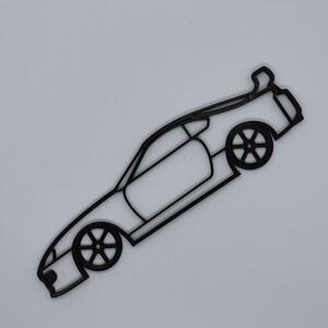 May include: Black line art silhouette of a sports car with a rear spoiler. The car is facing the right side of the image and is angled slightly upward.