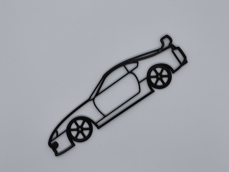 May include: Black line art silhouette of a sports car with a rear spoiler. The car is facing the right side of the image and is angled slightly upward.