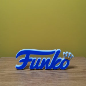 May include: Blue and white Funko logo with a gold crown on a wooden surface.