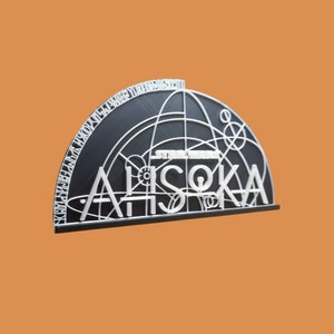 May include: A black and white 3D printed wall decor featuring the Star Wars character Ahsoka Tano's name in a stylized font. The background is a black circle with white lines and circles.