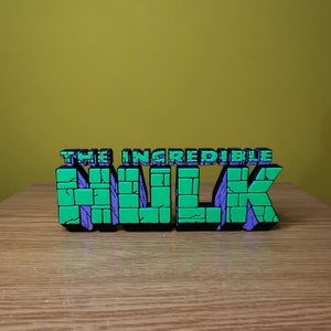 K&ouml;nnte beinhalten: Eine gr&uuml;ne und violette 3D-Wandskulptur mit den Worten "The Incredible Hulk" und einem Ziegelmuster.