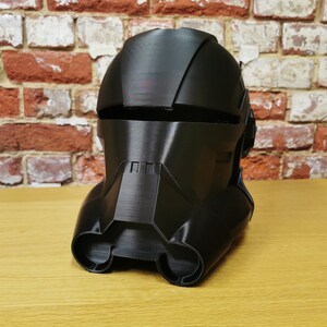 Puede incluir: Un casco de pl&aacute;stico negro con un dise&ntilde;o detallado, que se asemeja al casco de un soldado futurista.