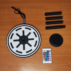 May include: A black and white round light with a Star Wars symbol, a remote control with color changing lights, and four black metal legs.
