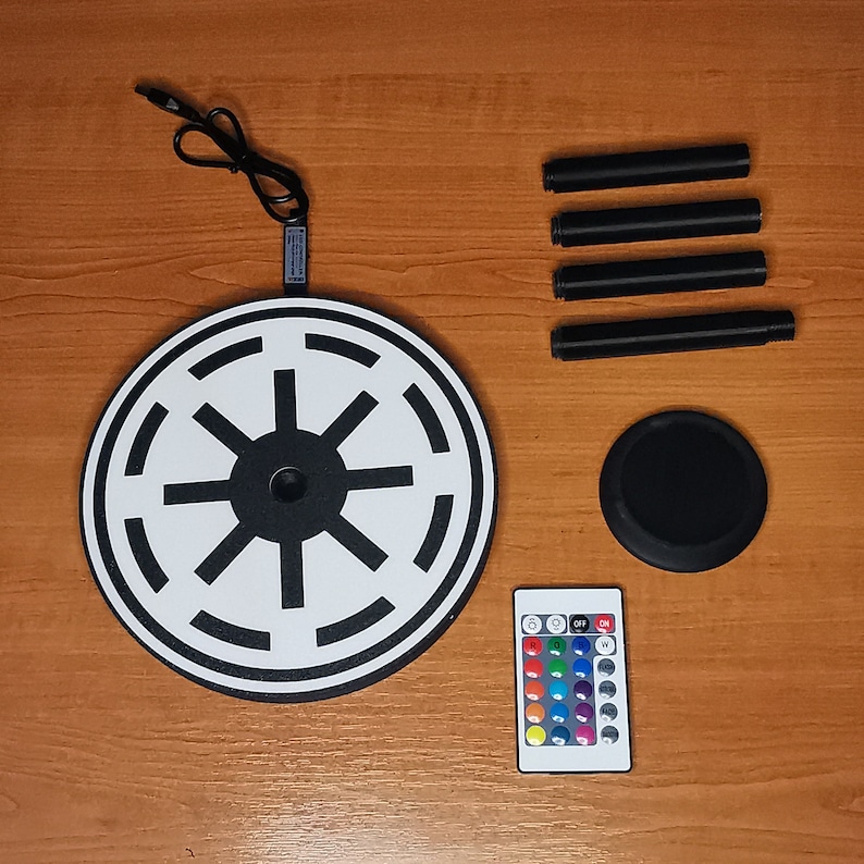 May include: A black and white round light with a Star Wars symbol, a remote control with color changing lights, and four black metal legs.