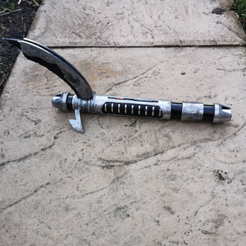 May include: A silver and black lightsaber with a broken handle. The lightsaber has a red button on the side and a black handle with a silver blade.