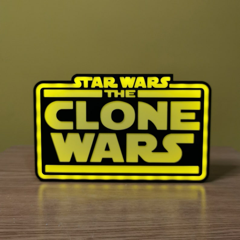 以下が含まれることがあります： 黒と黄色の看板に、太字の白いフォントで「スター・ウォーズ クローン・ウォーズ」と書かれています。