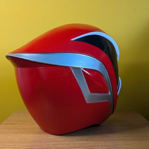 May include: Red and silver helmet with a black visor. The helmet is made of plastic and has a smooth, glossy finish.