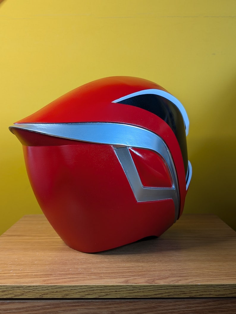 May include: Red and silver helmet with a black visor. The helmet is made of plastic and has a smooth, glossy finish.