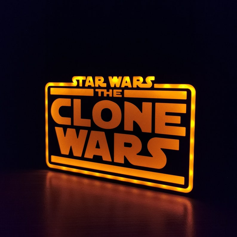 以下が含まれることがあります： 黒い長方形の枠の中に「STAR WARS THE CLONE WARS」という文字が書かれた、黄色く光る看板です。