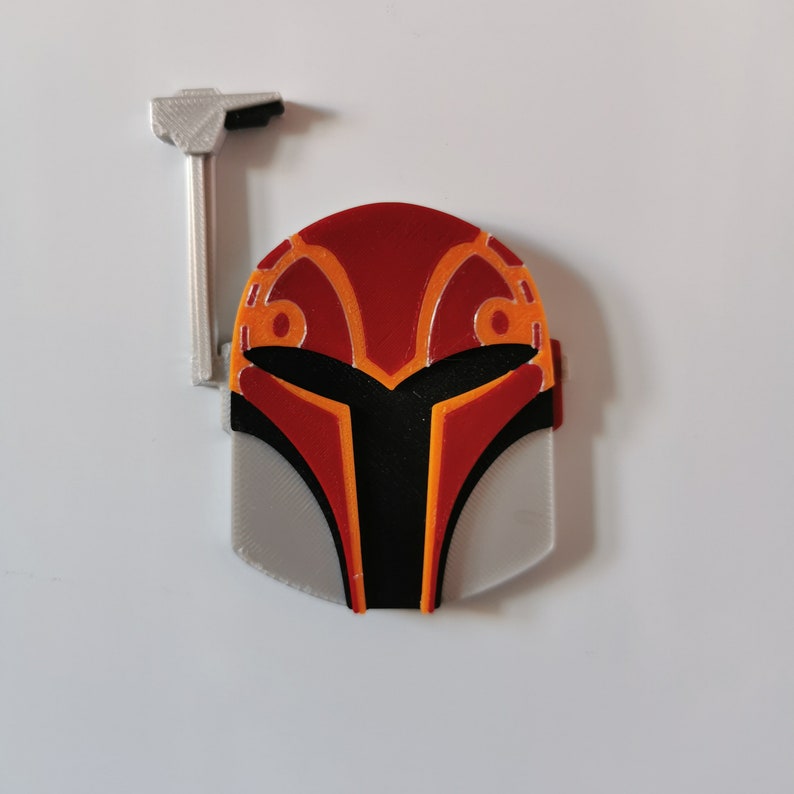 May include: A red and orange Mandalorian helmet with a gray visor and a silver attachment on top.
