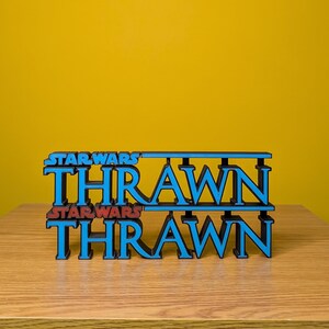 May include: A 3D printed model of the Star Wars character Thrawn's name in blue with the words "Star Wars" in red above and below the name.