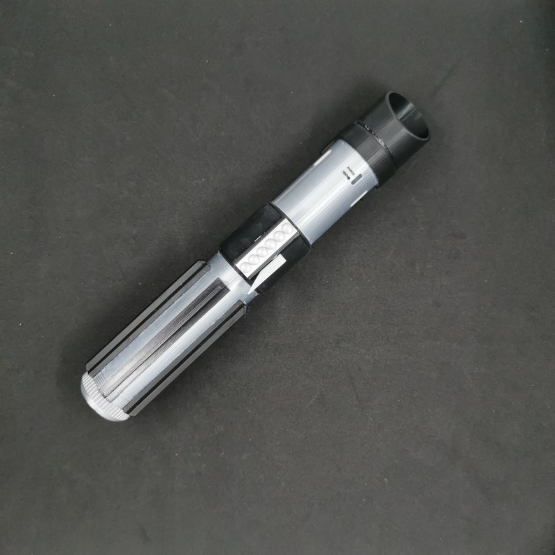 May include: A black and silver lightsaber toy with a textured handle and a black cap on the end.