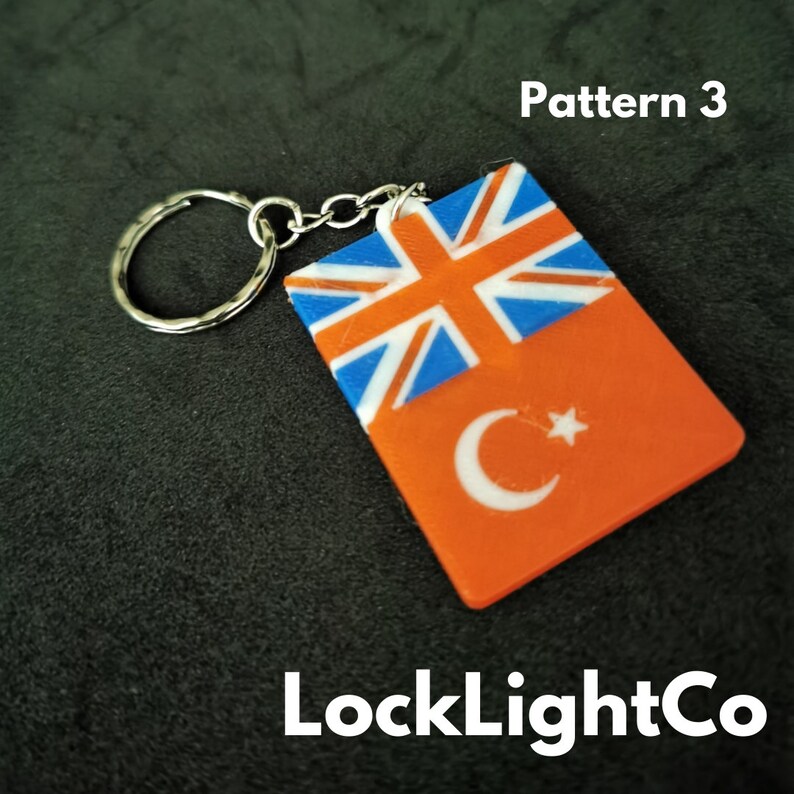 May include: A keychain with a red, white, and blue Union Jack flag on top of a red Turkish flag with a white crescent moon and star. The keychain is attached to a silver metal ring and chain. The text "Pattern 3" is visible above the keychain and "LockLightCo" is visible below the keychain.