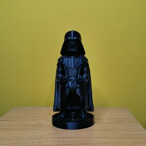 May include: A black Darth Vader figurine with a cape and lightsaber. The figurine is standing on a black base.