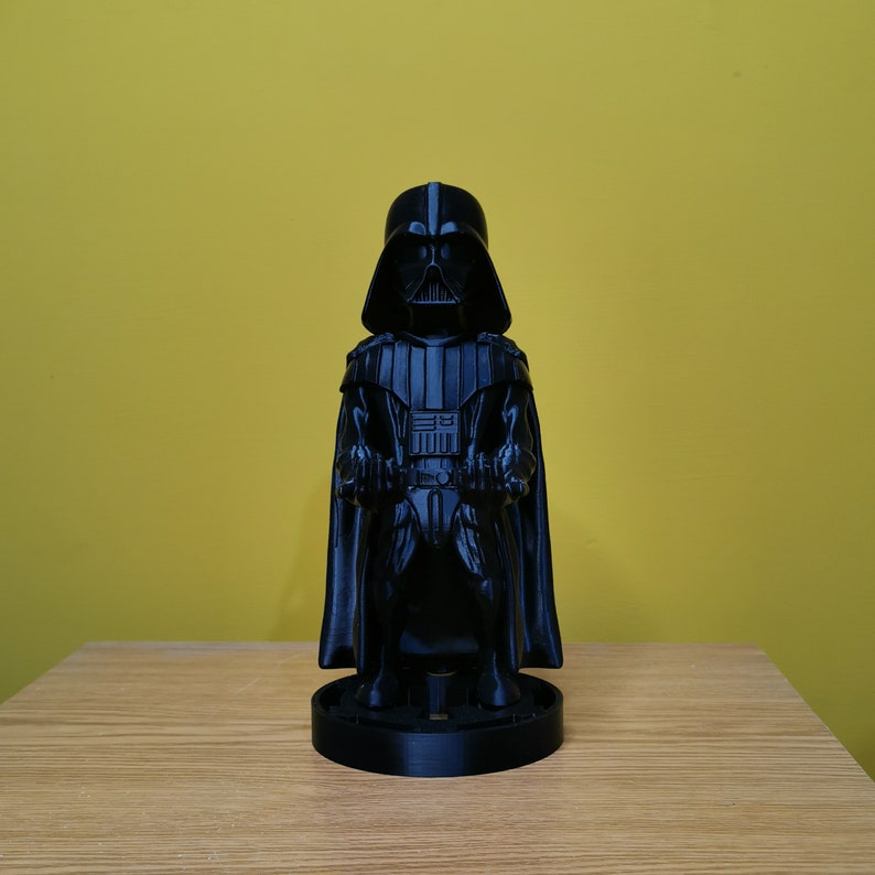 May include: A black Darth Vader figurine with a cape and lightsaber. The figurine is standing on a black base.