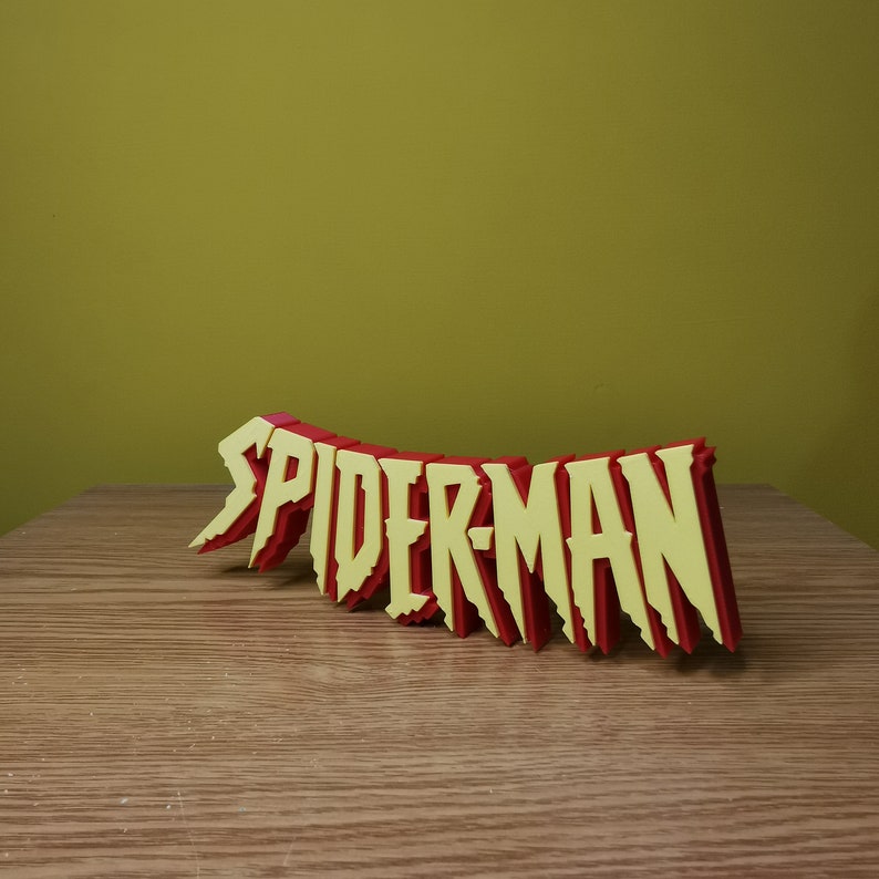 May include: A 3D printed sign that says "SPIDER-MAN" in red and yellow letters. The letters are stylized and have a jagged edge.