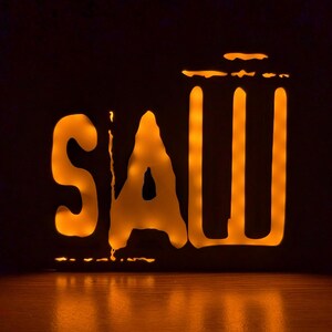 May include: A black and orange light-up sign with the word "SAW" and a silhouette of a trash can.
