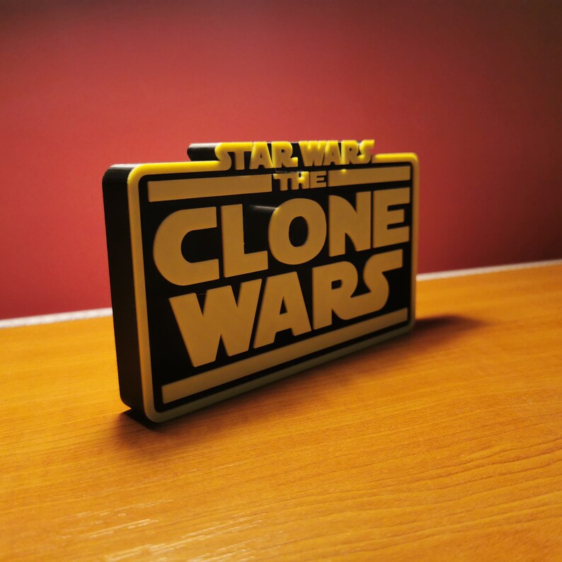 May include: A black and yellow 3D printed sign that reads "Star Wars The Clone Wars".