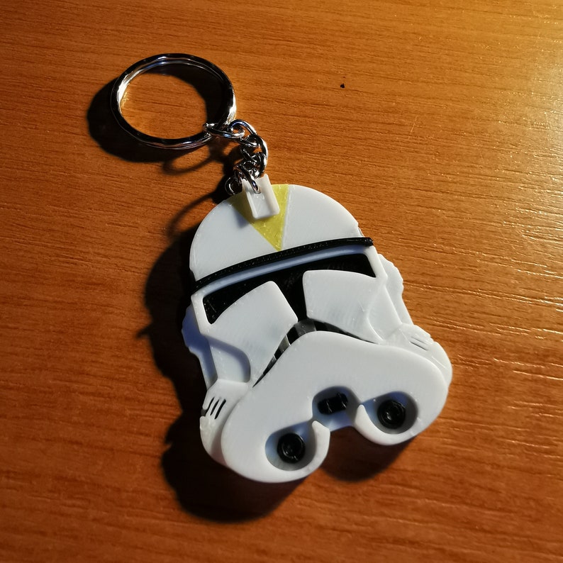 May include: White plastic keychain featuring a 3D printed clone trooper helmet with a yellow stripe on top.