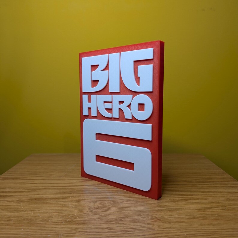 May include: A red and white 3D printed sign with the words "BIG HERO 6" in white raised letters.