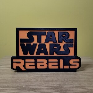 May include: A black and orange 3D printed sign with the text "Star Wars Rebels".