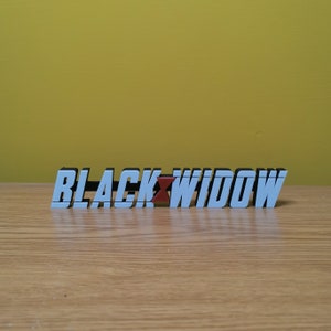 May include: A white plastic sign with the words "BLACK WIDOW" in black letters. A red widow symbol is between the words.