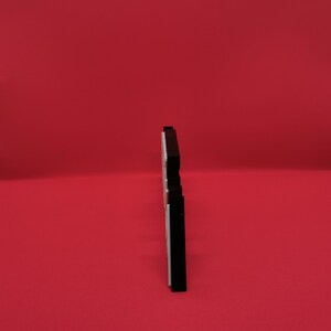 May include: A black and white decorative object, possibly a sign or plaque, stands against a solid red background. The object has a layered design with a black top and bottom, and a white center. The shape is stylized and modern.