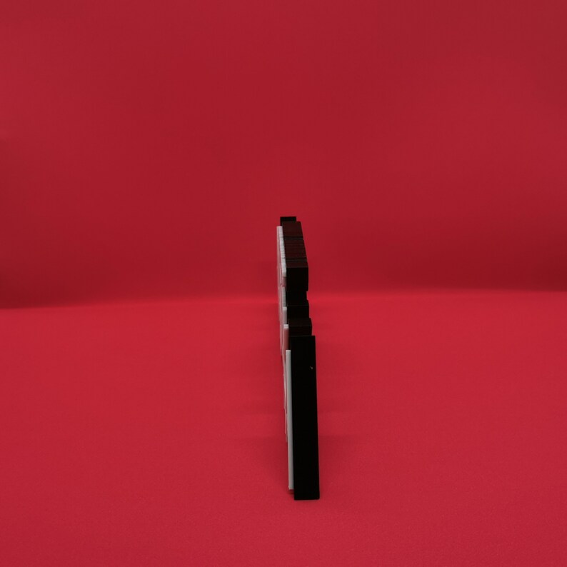 May include: A black and white decorative object, possibly a sign or plaque, stands against a solid red background. The object has a layered design with a black top and bottom, and a white center. The shape is stylized and modern.