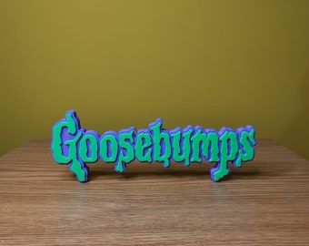 May include: A 3D printed sign in green and purple that reads "Goosebumps".