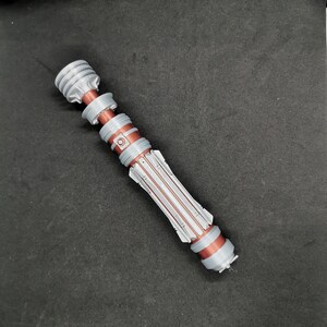 May include: A silver and copper lightsaber prop with a textured handle and a black tip.