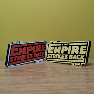 May include: Two 3D printed Star Wars: The Empire Strikes Back logos. The top logo is yellow and the bottom logo is red.