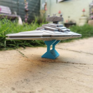 May include: A gray Star Destroyer model spaceship on a blue stand. The spaceship is a popular item in the Star Wars franchise.