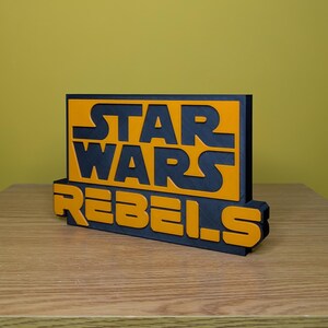 May include: A black and orange 3D printed sign with the text "STAR WARS REBELS".