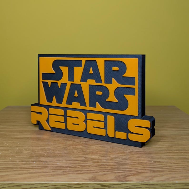 May include: A black and orange 3D printed sign with the text "STAR WARS REBELS".