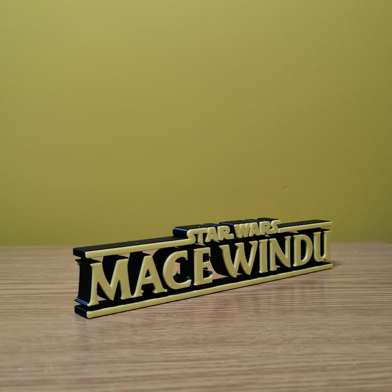 May include: A black and yellow 3D printed sign that reads "STAR WARS MACE WINDU".