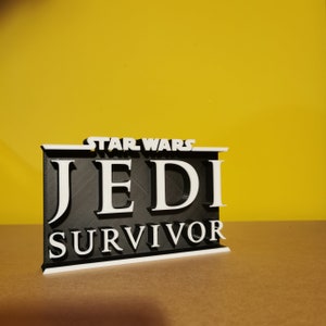 May include: A black and white 3D printed sign with the text "STAR WARS JEDI SURVIVOR" in white letters on a black background.