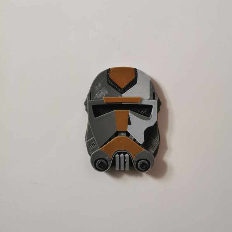 May include: A 3D printed helmet in gray, white, and gold. The helmet has a visor and a mouth guard.