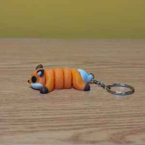 May include: A small orange and white fox keychain with a curled body and a silver key ring.