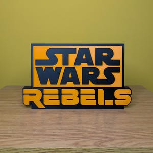 May include: A black and orange 3D printed sign with the text "STAR WARS REBELS".