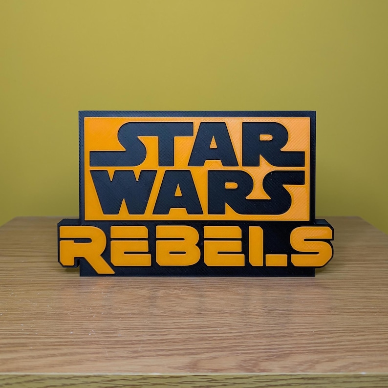May include: A black and orange 3D printed sign with the text "STAR WARS REBELS".