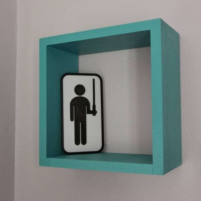 Pu&ograve; includere: Una cornice in legno blu turchese con un cartello bianco all'interno. Il cartello presenta una silhouette nera di una persona che tiene un bastone.