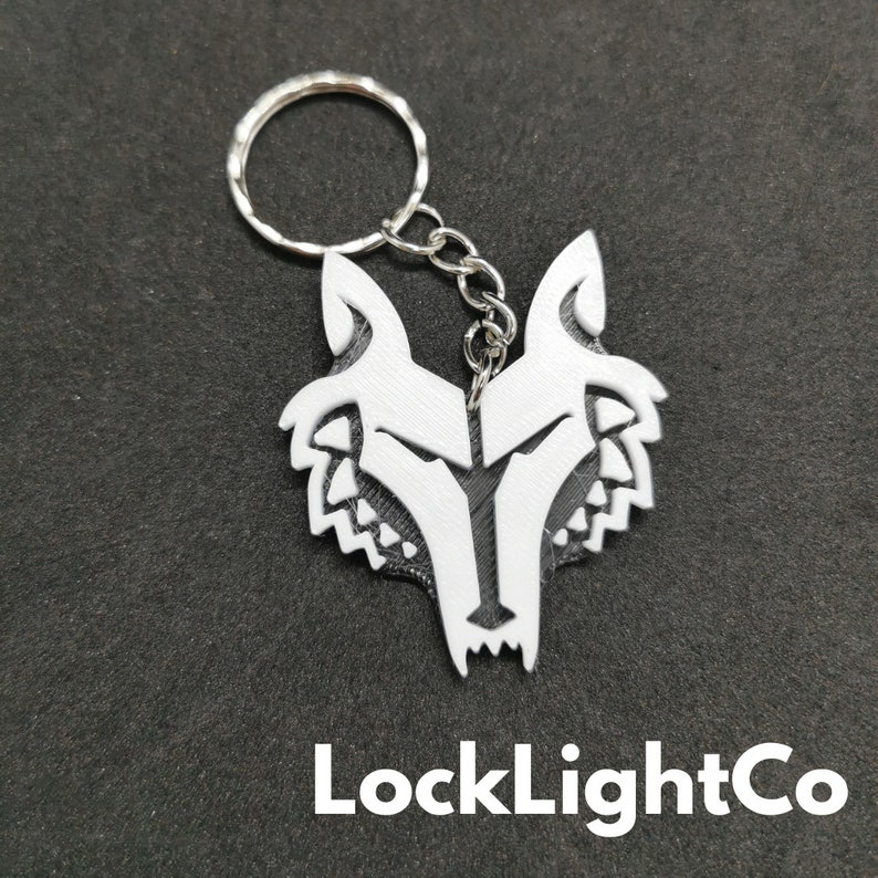 May include: White wolf head keychain with a silver chain and ring. The wolf head is a stylized design with a detailed face and fur. The keychain is labeled "LockLightCo".