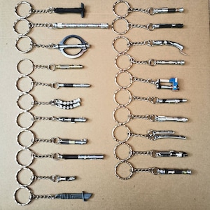 Op de afbeelding: Een verzameling van 18 zilveren sleutelhangers met verschillende Star Wars lightsaber-ontwerpen. Elke sleutelhanger heeft een zilveren ring en een zilveren ketting die is bevestigd aan een miniatuur lightsaber-replica.